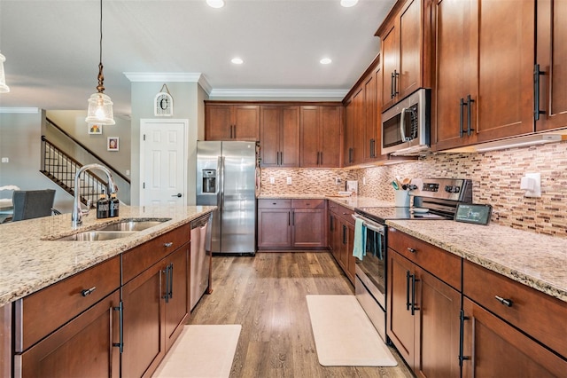 kitchen featuring appliances with stainless steel finishes, a sink, ornamental molding, light wood finished floors, and light stone countertops