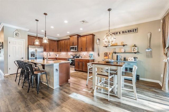 kitchen featuring appliances with stainless steel finishes, a sink, brown cabinetry, backsplash, and wood finished floors