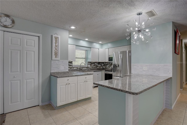 kitchen featuring appliances with stainless steel finishes, decorative backsplash, a peninsula, white cabinets, and light tile patterned floors