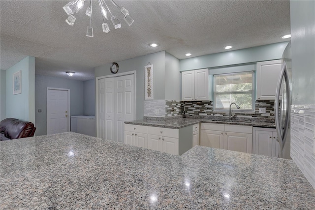 kitchen featuring a sink, white cabinetry, dark stone countertops, a textured ceiling, and tasteful backsplash