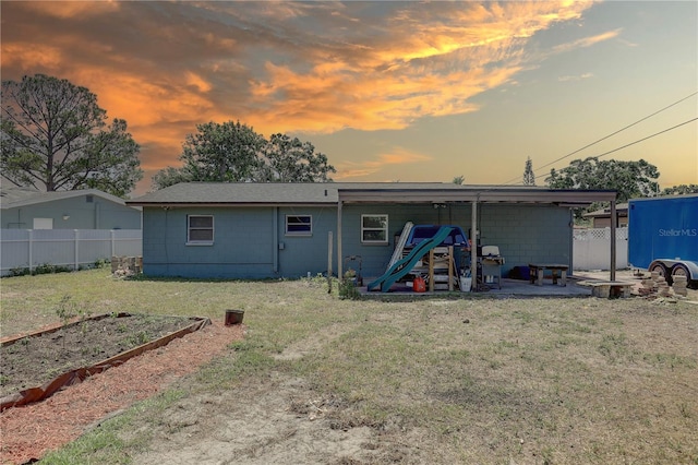 back of house at dusk featuring concrete block siding, a vegetable garden, and an attached carport