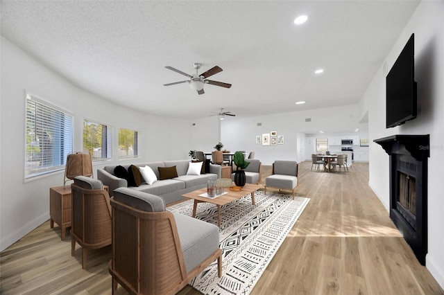 living area featuring light wood-type flooring, ceiling fan, a glass covered fireplace, recessed lighting, and baseboards