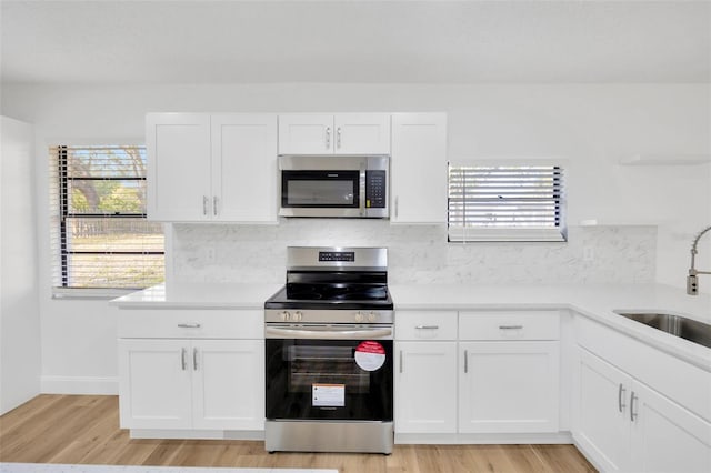 kitchen with stainless steel appliances, a sink, light countertops, light wood finished floors, and white cabinetry