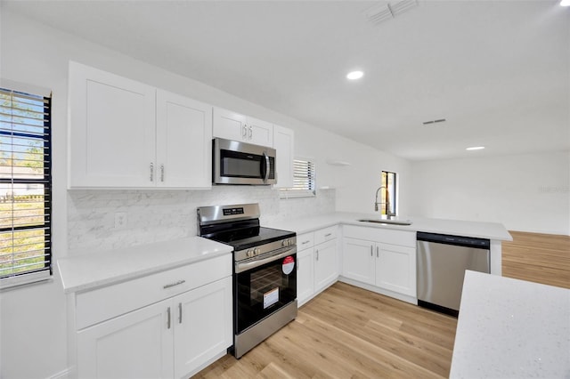 kitchen featuring stainless steel appliances, a sink, decorative backsplash, light wood-style floors, and recessed lighting
