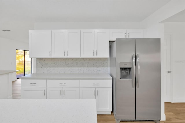 kitchen featuring stainless steel fridge, white cabinetry, light countertops, light wood-type flooring, and backsplash