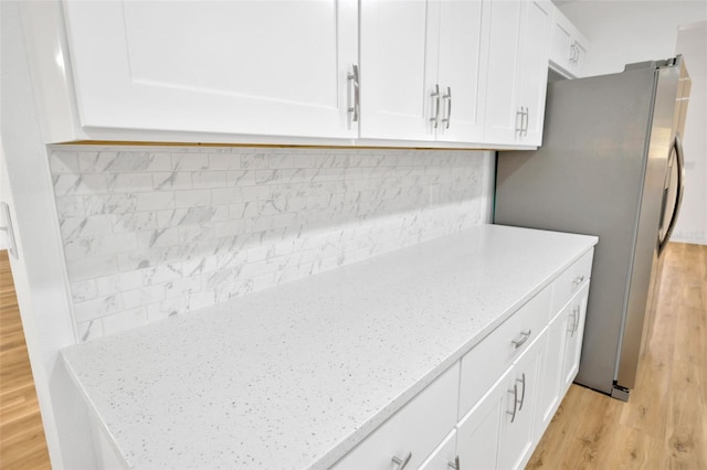 kitchen with light wood-style flooring, white cabinetry, decorative backsplash, and light stone countertops