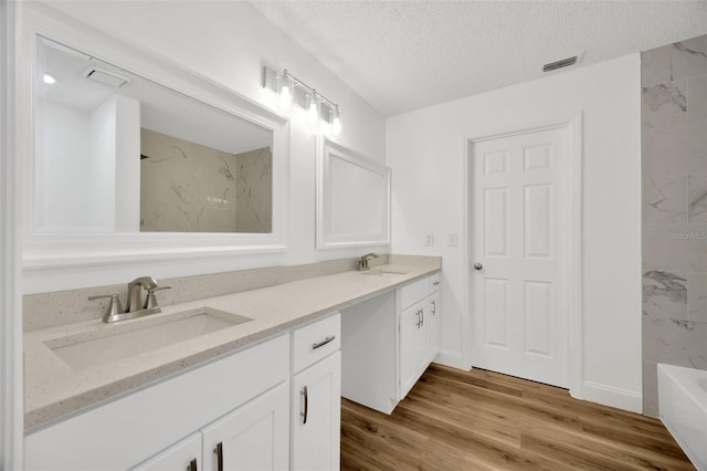 full bathroom featuring a bathtub, a textured ceiling, double vanity, wood finished floors, and baseboards