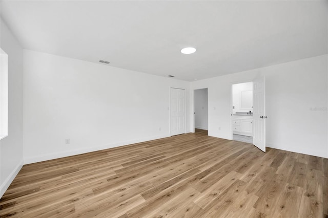 unfurnished bedroom featuring light wood-type flooring, ensuite bathroom, and baseboards