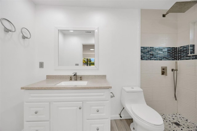 bathroom featuring a tile shower, toilet, vanity, and wood finished floors
