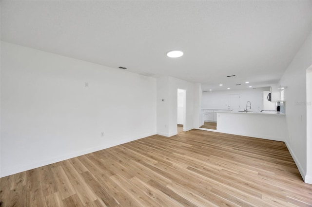 unfurnished living room with light wood-style flooring, a sink, recessed lighting, and baseboards