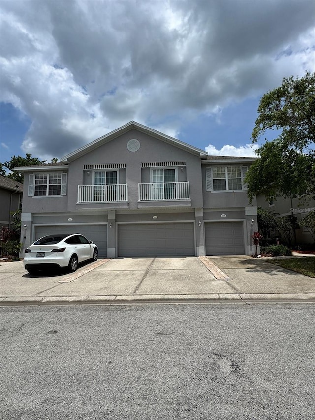 view of front facade with an attached garage, stucco siding, driveway, and a balcony