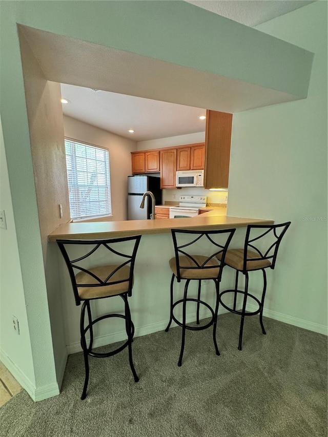kitchen with white appliances, carpet floors, a peninsula, a breakfast bar, and recessed lighting