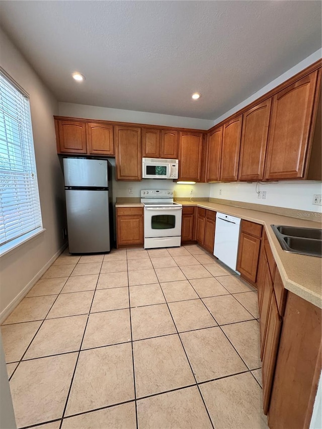 kitchen with white appliances, a sink, brown cabinetry, and recessed lighting