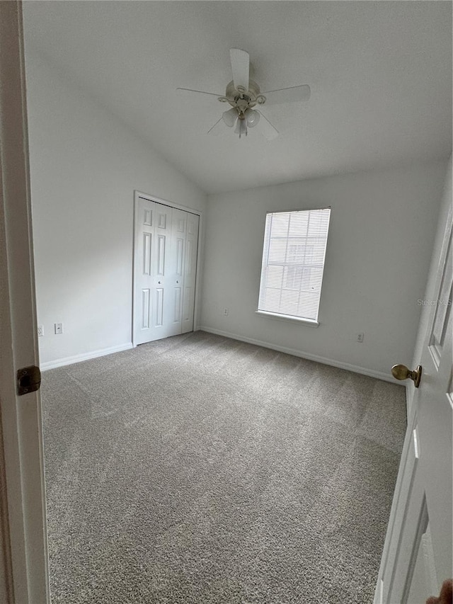 unfurnished bedroom featuring carpet flooring, baseboards, vaulted ceiling, a closet, and a ceiling fan