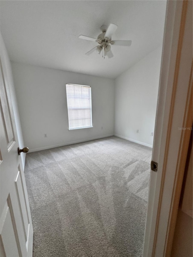 carpeted spare room featuring ceiling fan and baseboards