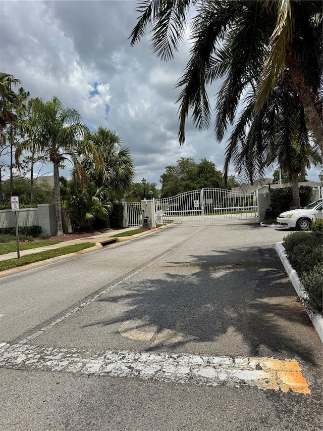 view of asphalt road with a gate, sidewalks, curbs, and a gated entry