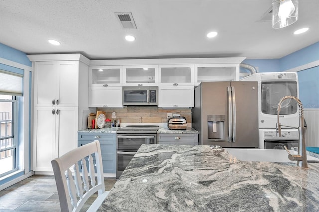 8931 Blind Pass Rd Unit 360, St Pete Beach, FL 33706 - kitchen featuring stainless steel appliances, stacked washer / drying machine, tasteful backsplash, white cabinets, and recessed lighting