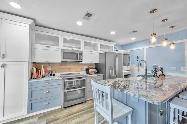 8931 Blind Pass Rd Unit 360, St Pete Beach, FL 33706 - kitchen with stacked washer / dryer, stainless steel appliances, a kitchen bar, light wood finished floors, and white cabinetry