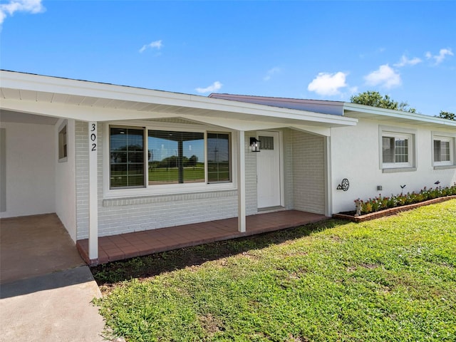 302 Patty Dr, Oldsmar, FL 34677 - doorway to property with a lawn, covered porch, brick siding, and stucco siding