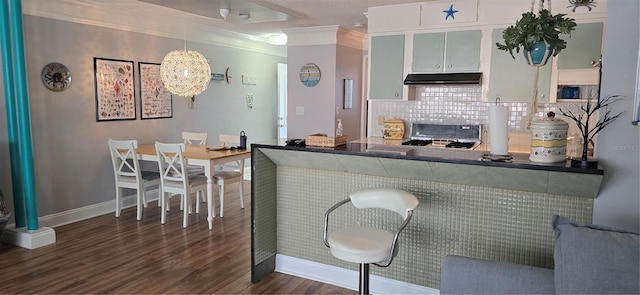 kitchen featuring under cabinet range hood, dark wood-type flooring, ornamental molding, tasteful backsplash, and stove