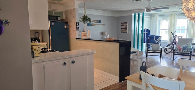 kitchen featuring fridge, black microwave, a peninsula, ceiling fan, and a textured ceiling