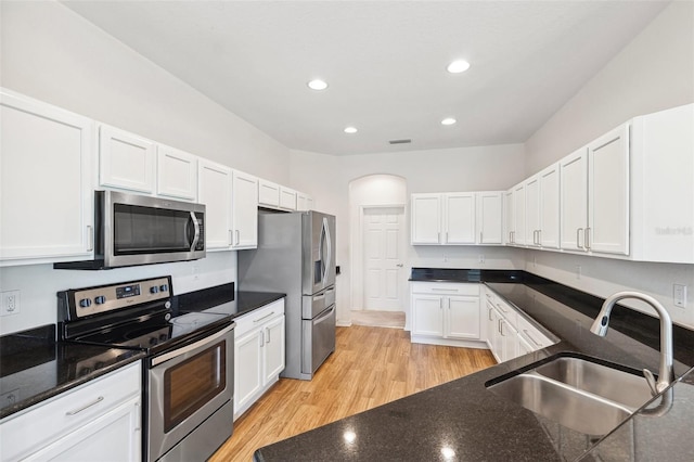 kitchen with appliances with stainless steel finishes, a sink, light wood-type flooring, white cabinetry, and recessed lighting