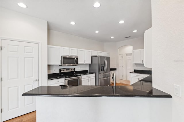kitchen with stainless steel appliances, arched walkways, recessed lighting, white cabinets, and light wood-style floors