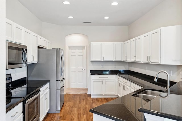 kitchen with stainless steel appliances, a sink, white cabinets, dark stone countertops, and light wood finished floors