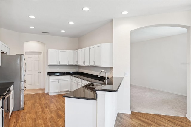 kitchen featuring a sink, arched walkways, white cabinetry, dark countertops, and light wood-type flooring