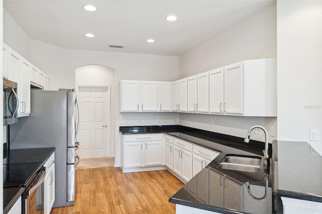 kitchen with a sink, electric range oven, stainless steel microwave, light wood-type flooring, and white cabinetry