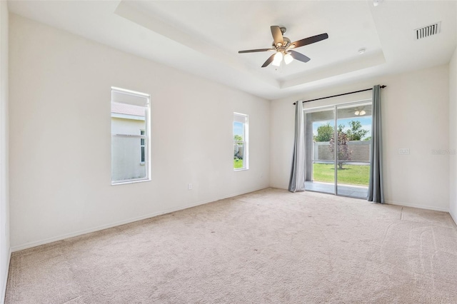 carpeted spare room featuring a tray ceiling, ceiling fan, and baseboards