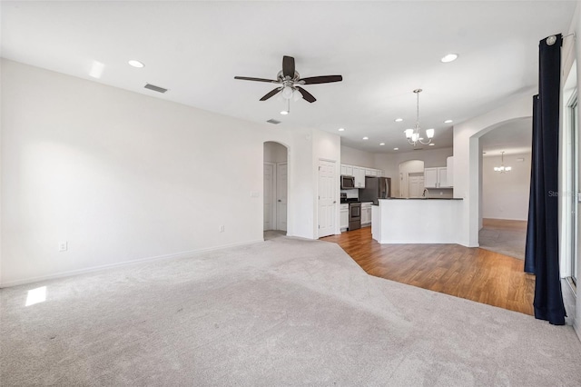unfurnished living room featuring light carpet, a chandelier, arched walkways, a ceiling fan, and baseboards
