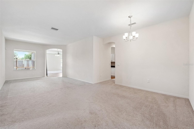 spare room featuring arched walkways, a chandelier, carpet floors, and baseboards