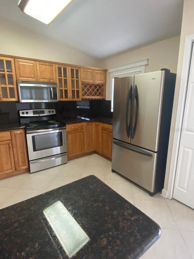 11014 Peking Pl, Tampa, FL 33624 - kitchen with appliances with stainless steel finishes, light tile patterned flooring, brown cabinetry, glass insert cabinets, and dark stone countertops
