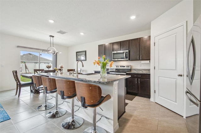 33524 Elm Hill Br, Wesley Chapel, FL 33545 - kitchen featuring appliances with stainless steel finishes, a sink, a breakfast bar area, a kitchen island with sink, and light stone counters
