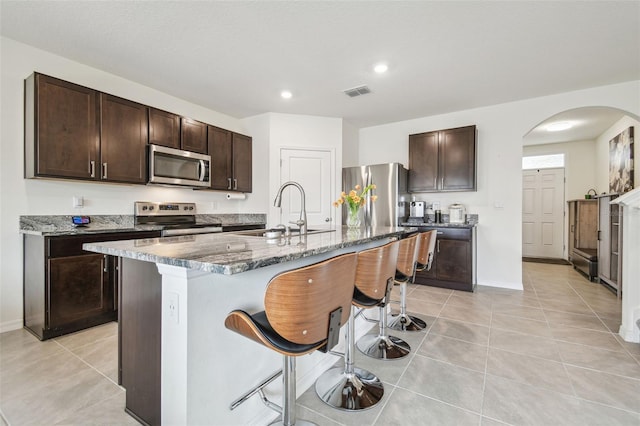 33524 Elm Hill Br, Wesley Chapel, FL 33545 - kitchen with stainless steel appliances, a sink, arched walkways, a kitchen breakfast bar, and dark brown cabinets