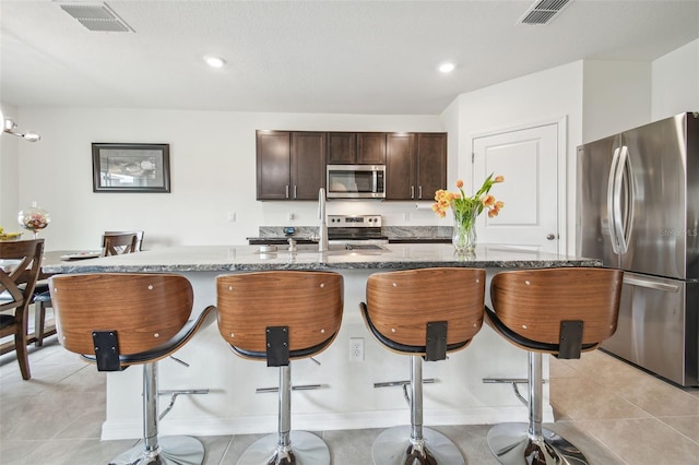 33524 Elm Hill Br, Wesley Chapel, FL 33545 - kitchen with stainless steel appliances, a breakfast bar, light tile patterned floors, dark stone counters, and recessed lighting