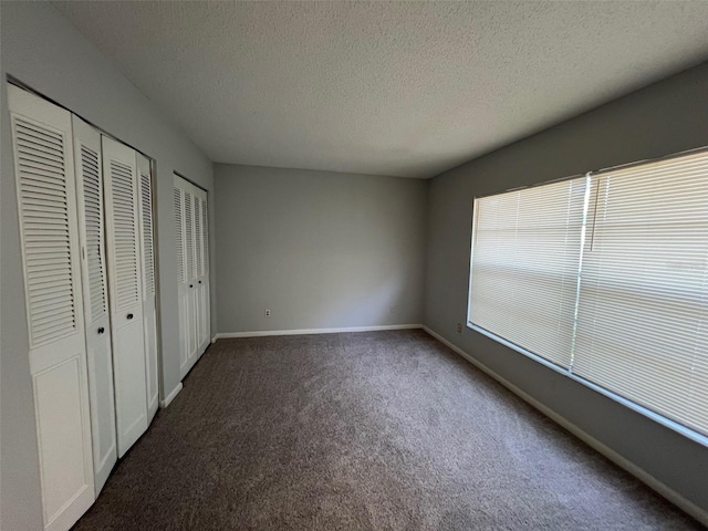 14725 Morning Dr, Lutz, FL 33559 - unfurnished bedroom with multiple closets, dark colored carpet, a textured ceiling, and baseboards