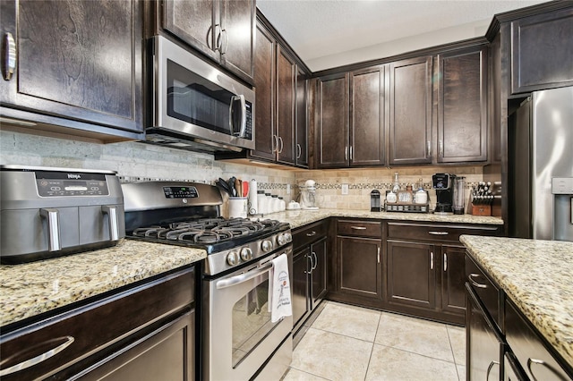 3530 Brook Crossing Dr, Brandon, FL 33511 - kitchen with appliances with stainless steel finishes, light tile patterned floors, light stone countertops, dark brown cabinets, and backsplash