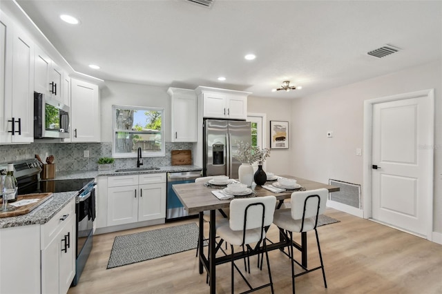 5624 62nd St N, Saint Petersburg, FL 33709 - kitchen with appliances with stainless steel finishes, a sink, backsplash, light wood-style flooring, and white cabinetry
