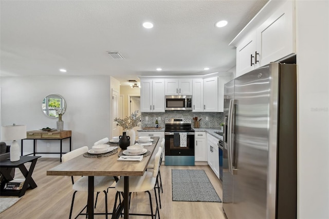 5624 62nd St N, Saint Petersburg, FL 33709 - kitchen with stainless steel appliances, white cabinets, decorative backsplash, light wood-type flooring, and recessed lighting