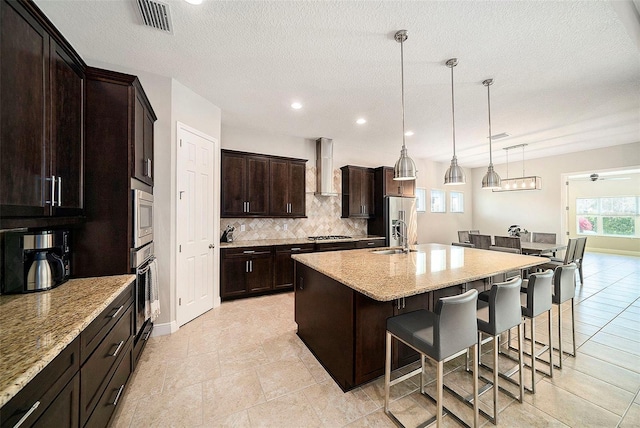 8016 Rock Spring Ct, Land O Lakes, FL 34638 - kitchen featuring stainless steel appliances, wall chimney range hood, a breakfast bar area, backsplash, and an island with sink