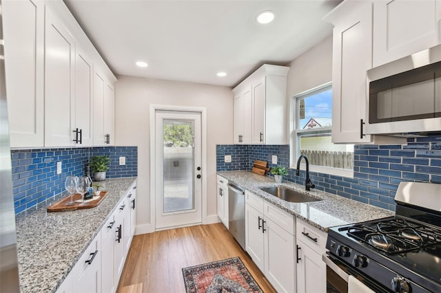 1750 Dayton St S, Saint Petersburg, FL 33712 - kitchen with appliances with stainless steel finishes, a sink, light wood-style flooring, white cabinets, and decorative backsplash