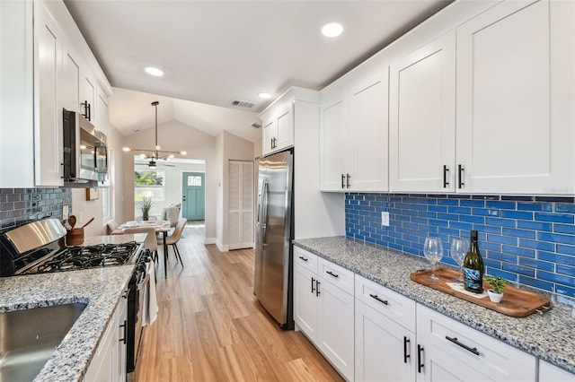 1750 Dayton St S, Saint Petersburg, FL 33712 - kitchen with stainless steel appliances, white cabinetry, light wood-style floors, vaulted ceiling, and tasteful backsplash
