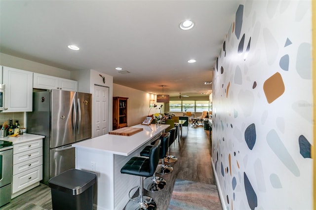 3850 13th Ave N Unit 113, Saint Petersburg, FL 33713 - kitchen featuring appliances with stainless steel finishes, white cabinets, a kitchen island, a kitchen breakfast bar, and light countertops
