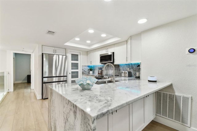 9812 Indian Key Trl Unit 84, Seminole, FL 33776 - kitchen featuring appliances with stainless steel finishes, a peninsula, a tray ceiling, light stone countertops, and white cabinetry