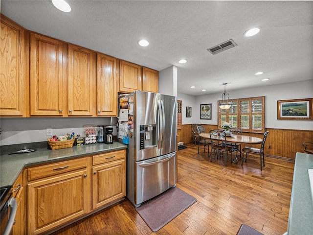 16326 Kalli Way, Dade City, FL 33523 - kitchen with appliances with stainless steel finishes, a wainscoted wall, dark countertops, brown cabinetry, and hardwood / wood-style floors