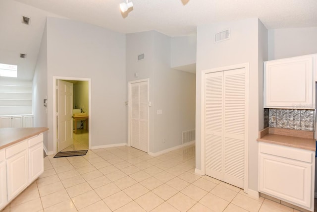 24 Lake Vista Way, Ormond Beach, FL 32174 - kitchen with high vaulted ceiling, white cabinetry, backsplash, light countertops, and light tile patterned flooring