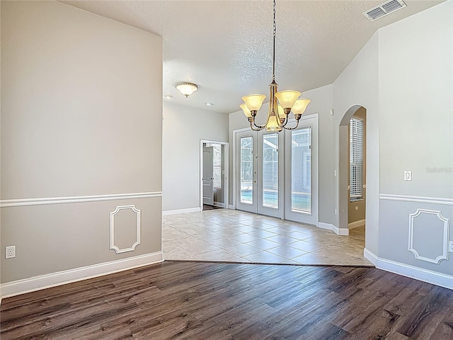 13110 Manistee Rd, Weeki Wachee, FL 34614 - unfurnished dining area featuring wood finished floors, a chandelier, a textured ceiling, baseboards, and arched walkways