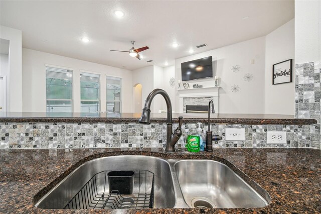 7410 Ambleside Dr, Land O Lakes, FL 34637 - kitchen view of a sink, ceiling fan, a fireplace, dark stone counters, and backsplash